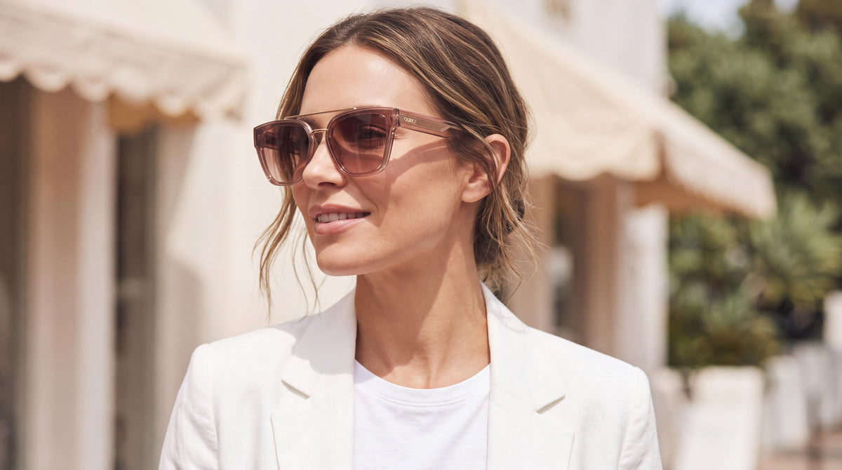 A woman's head-and-shoulders portrait, wearing a white linen blazer, smiling confidently in womens quay oversized square sunglasses.