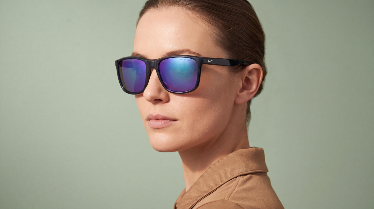 A sophisticated young woman in a performance polo wearing womens nike polarized mirrored sunglasses in a soft sage-green studio.