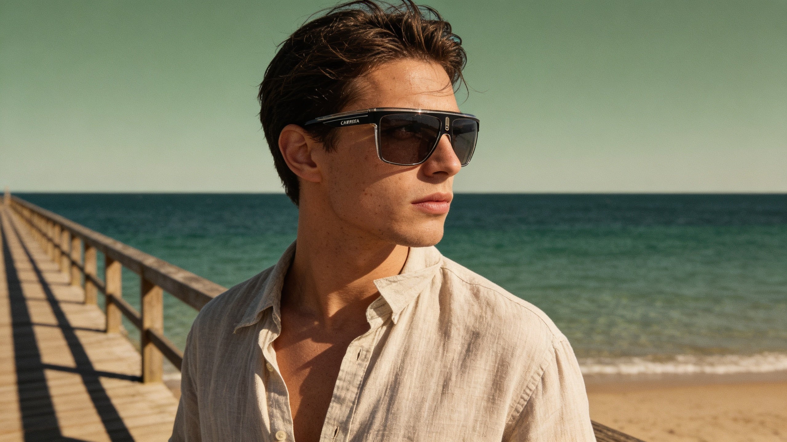 Stylish person on boardwalk wearing Carrera polarized sunglasses, gazing at a clear ocean horizon, perfect for road trips